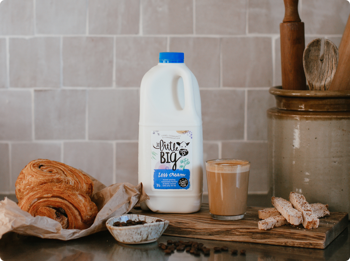 Little Big Dairy Less Cream Milk in a 2L bottle on kitchen bench with pastries.