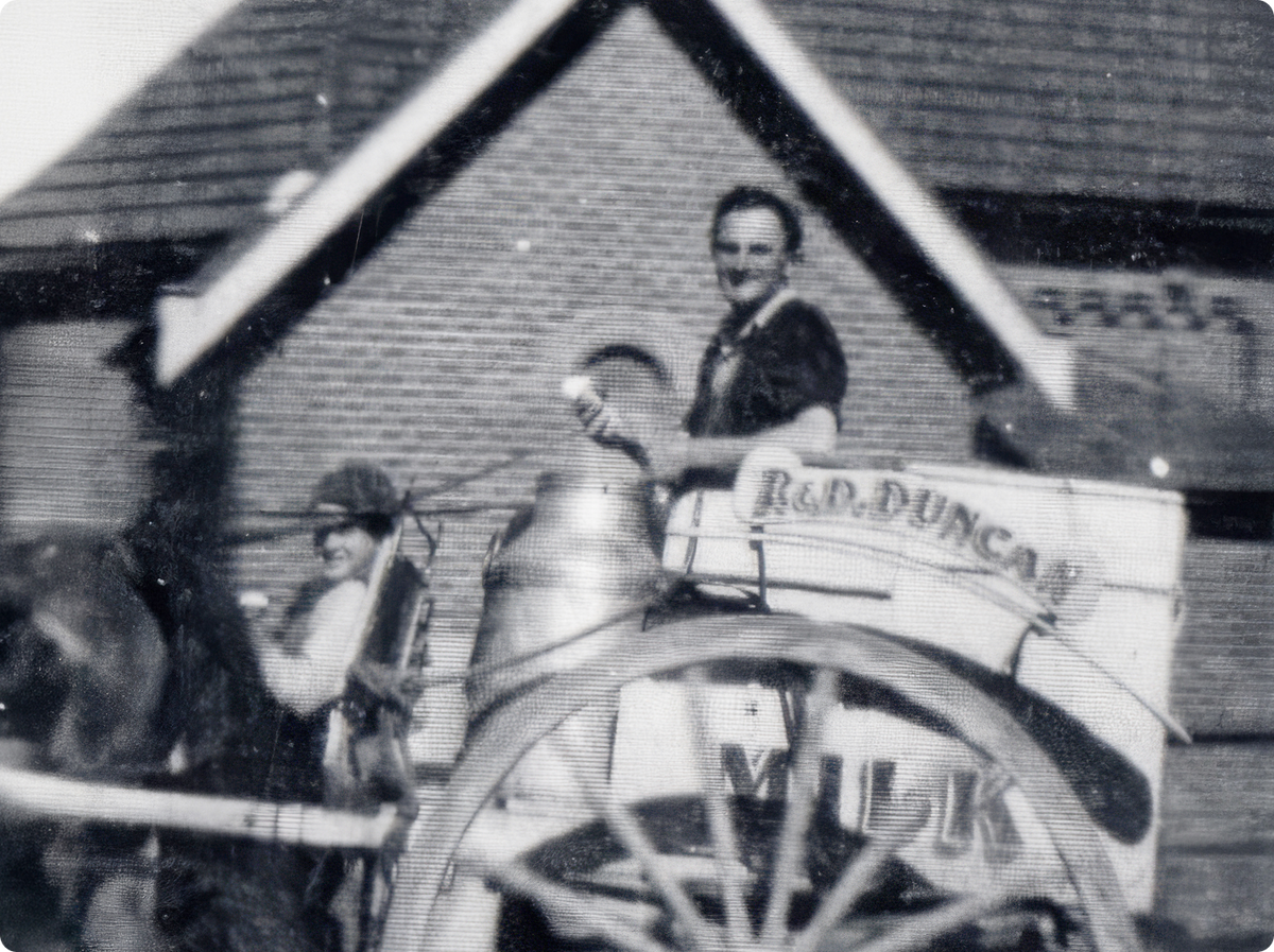 Black and white vintage photograph showing a horse-drawn cart with a smiling man seated at the back.